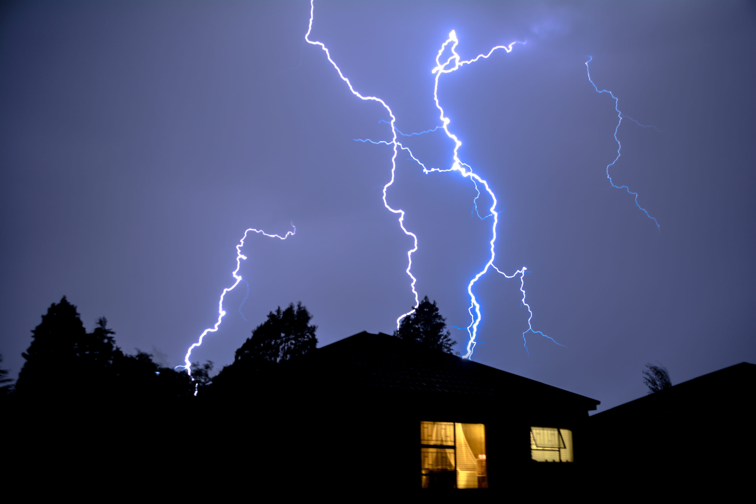 A lightning strike lights up the sky behind a residential home during a storm