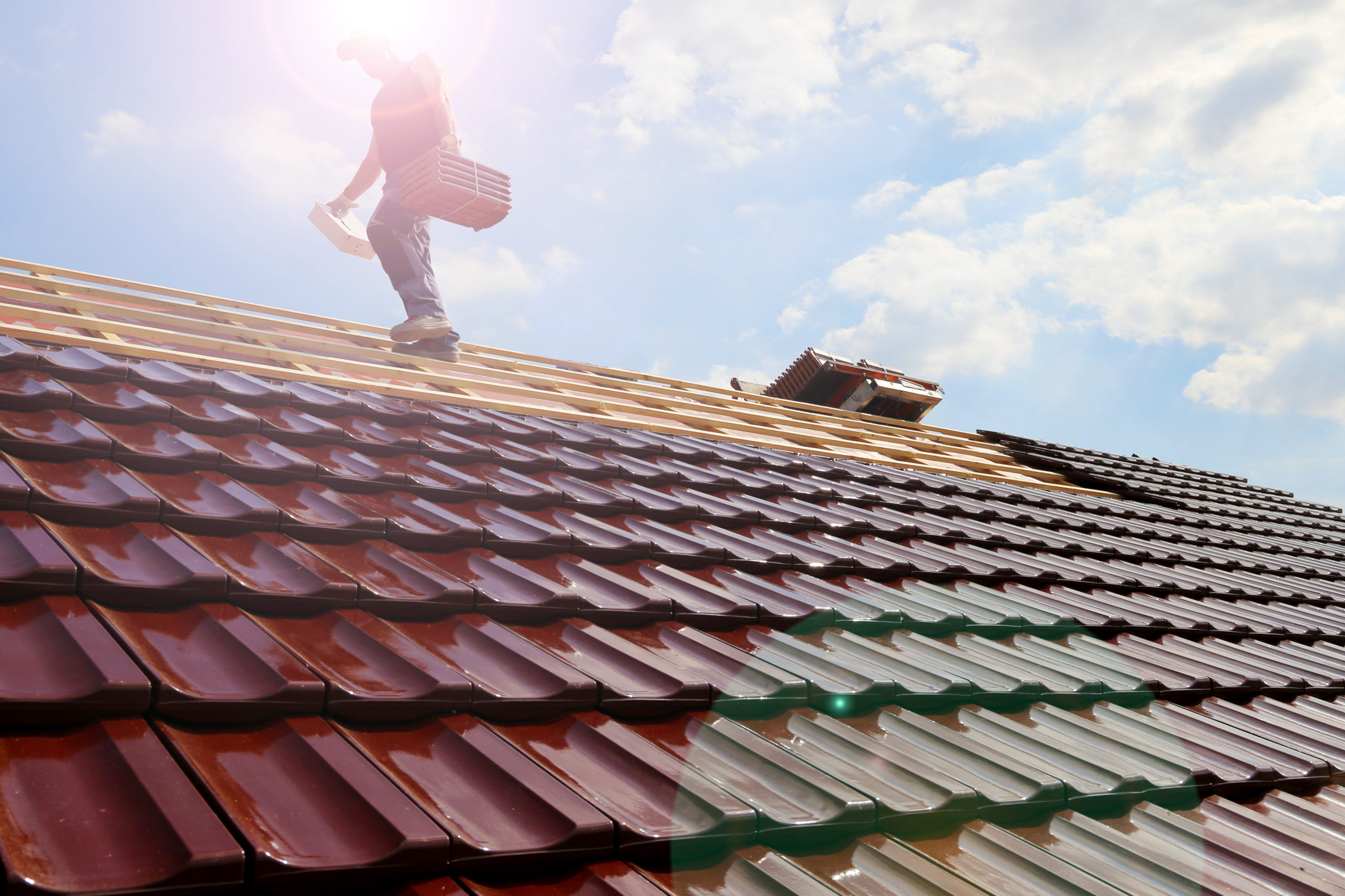 A contractor walks across a residential roof while installing new shingles.