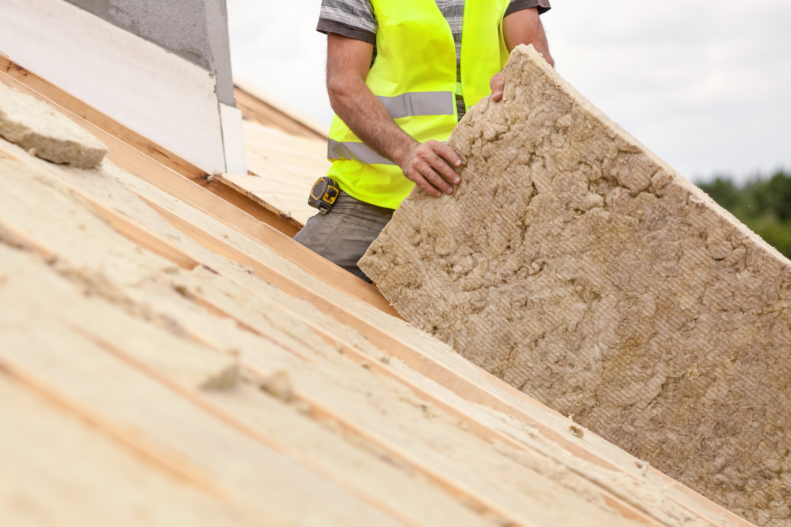 A roofing contractor stands in top of a residential roof while holding a piece of roofing insulation.