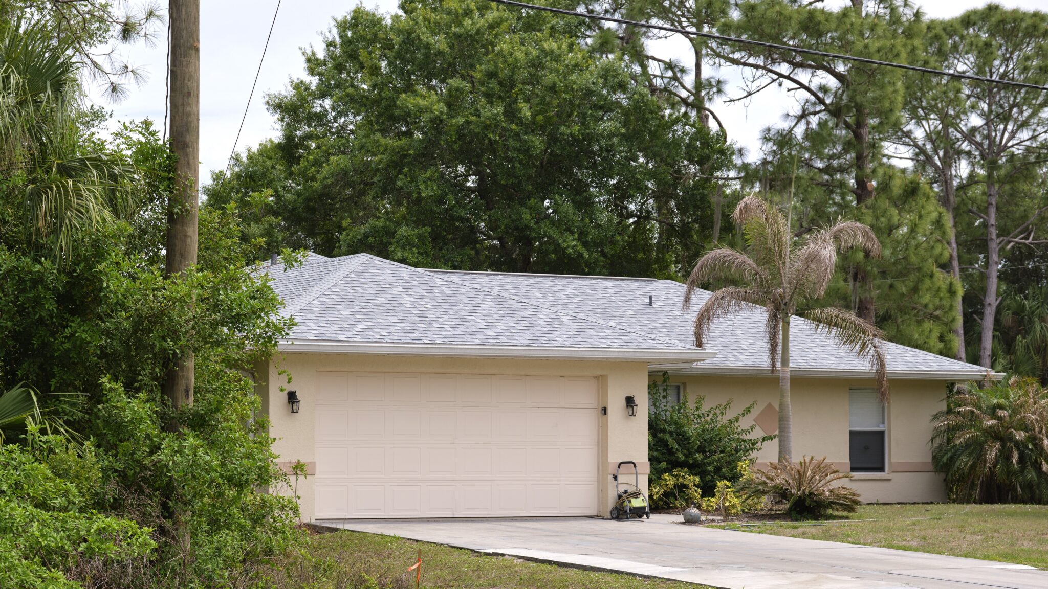 Florida home with grey cement exterior with  black stone-coated roof, black and grey tile driveway, and garage
