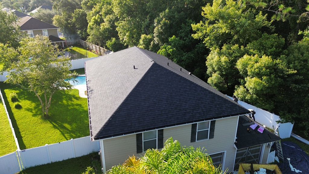 Aerial view of a home with an asphalt shingle roof surrounded by trees