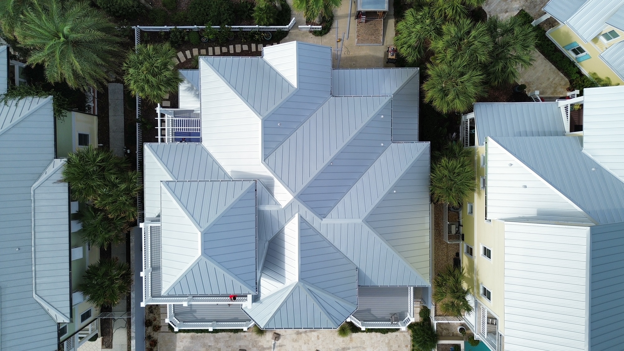 Aerial view of a large home  with white roof and palm trees