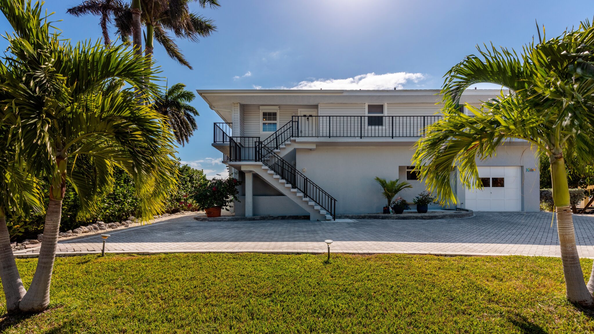 Perfect grey two-story Florida home with flat roof, staircase with black railing, with a small garage with white door with stucco driveway