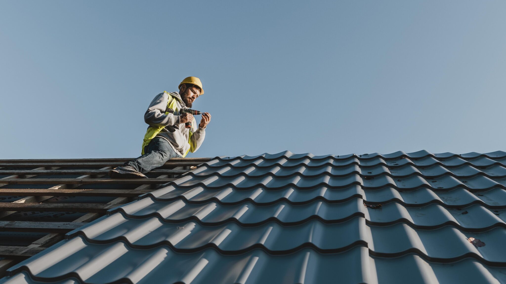 A roofer carefully installs metal roof panels decoratively shaped to imitate shingles
