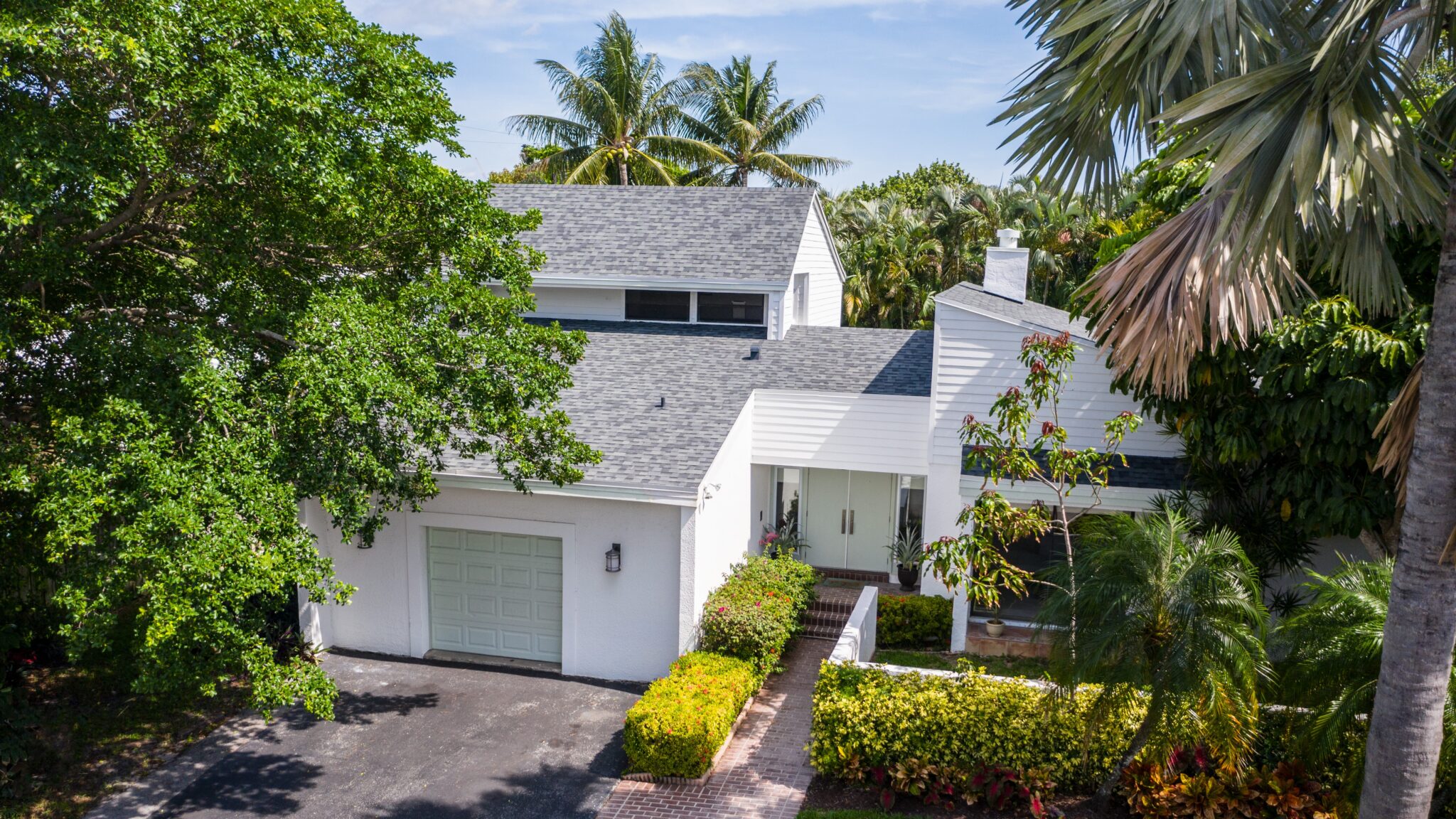 Aerial view of home with white exterior and grey asphalt shingled roof partly secluded by trees