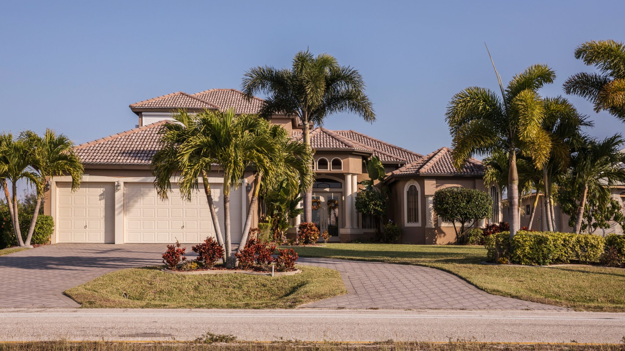 House with stucco siding and brown tile roof, palm trees in the front yard