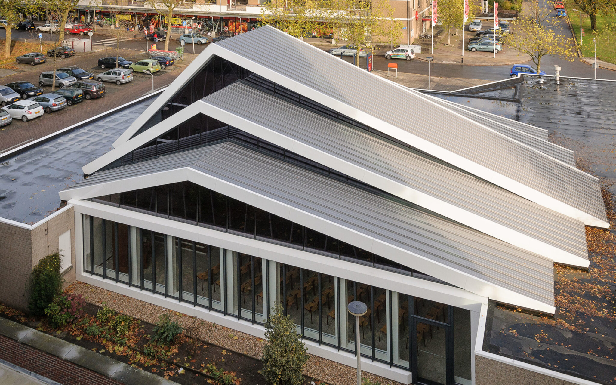 The image features a stylish commercial building with a metal roof. There is a parking lot filled with cars behind the building
