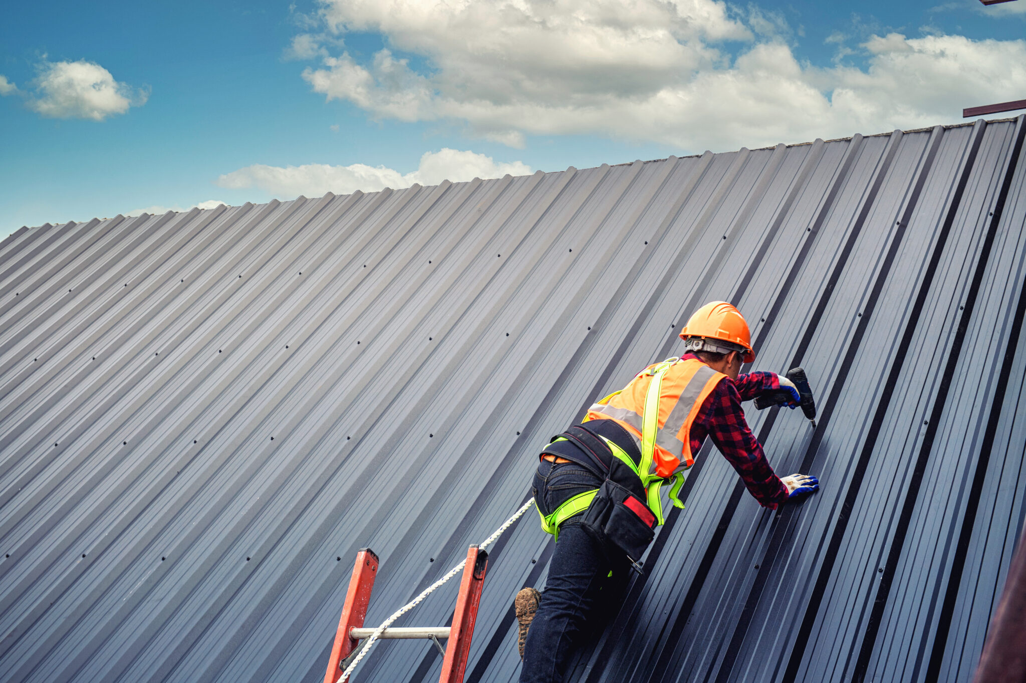 Man in hard hat on metal roof making repair