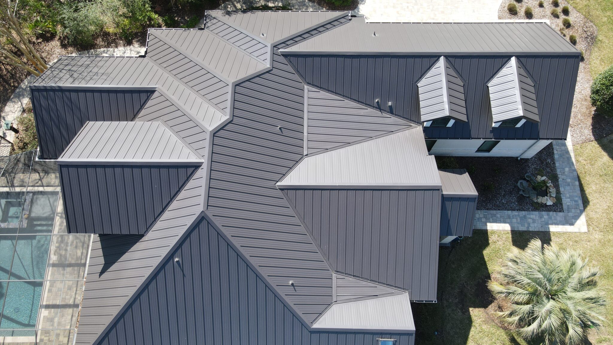Bird’s eye view of gray metal roof on Florida home with backyard pool and freshly trimmed landscaped yard