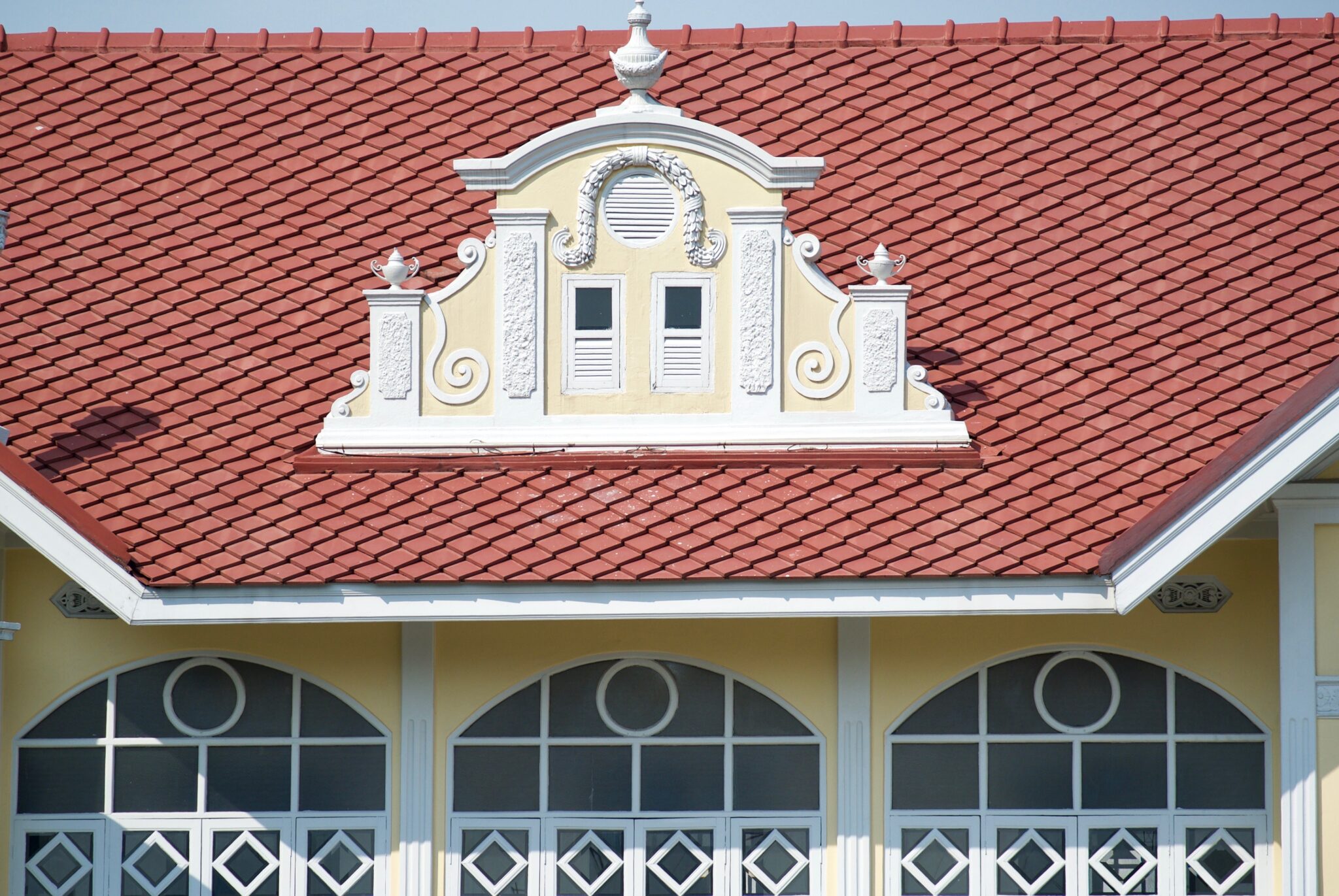 An ornate, red, Spanish roof on a white and yellow building