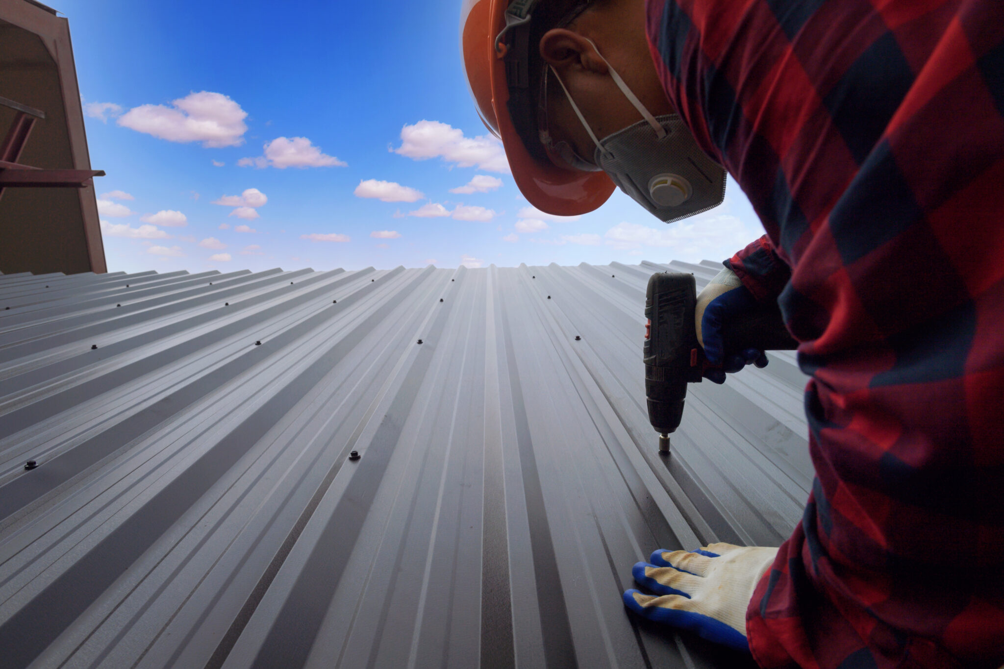 Image of a man installing a metal roof on a home against a blue, cloudy sky