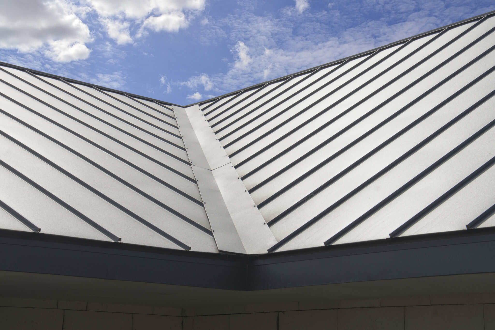Close-up image of a silver standing seam roof against a cloudy blue sky