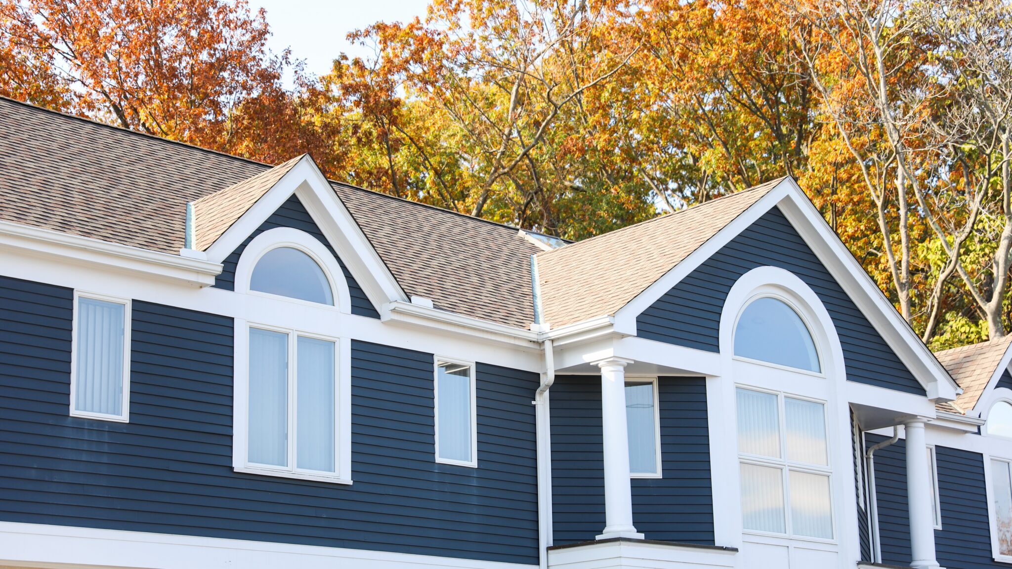 Home exterior with blue siding and windows with white frames with newly installed asphalt shingle roofing