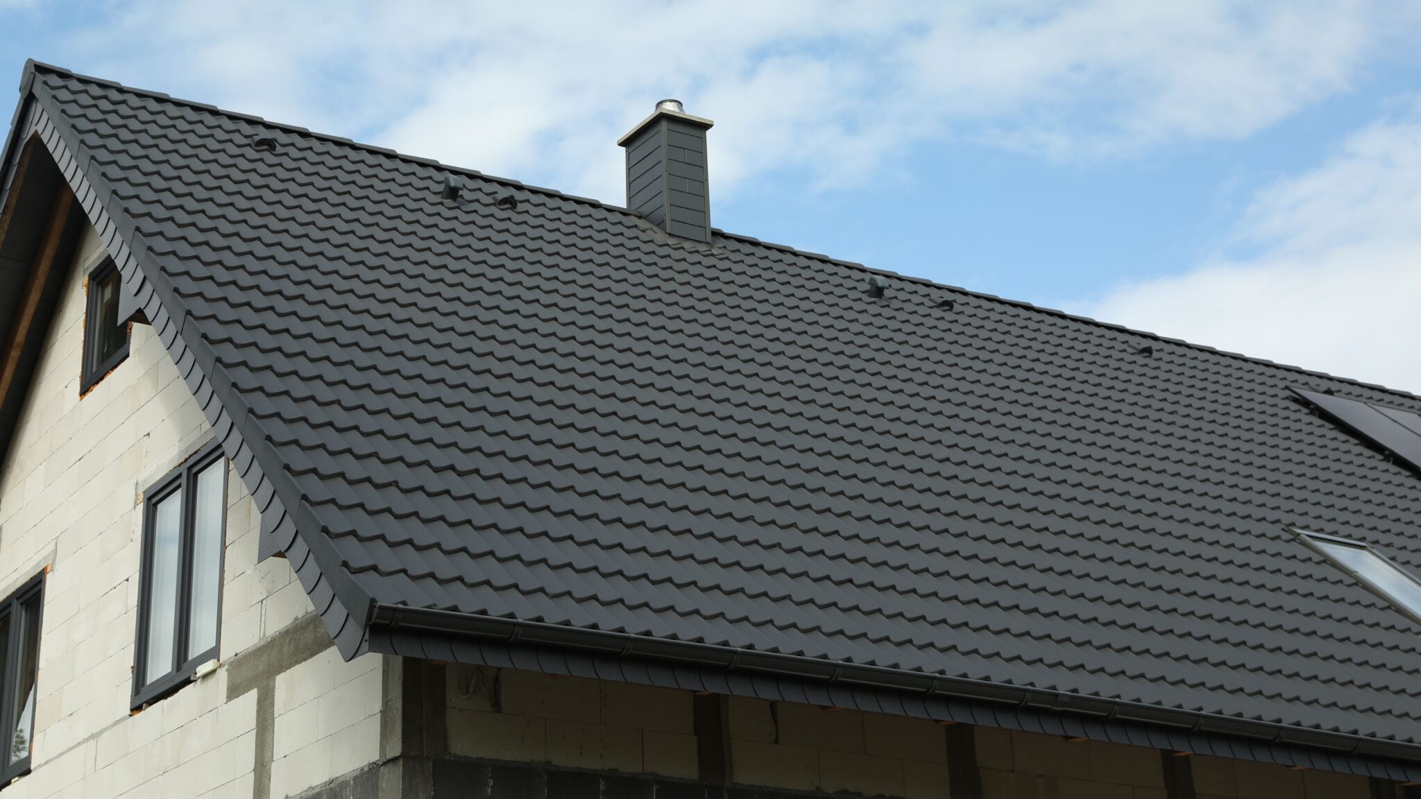 Large new dark metal roof on home with white brick siding