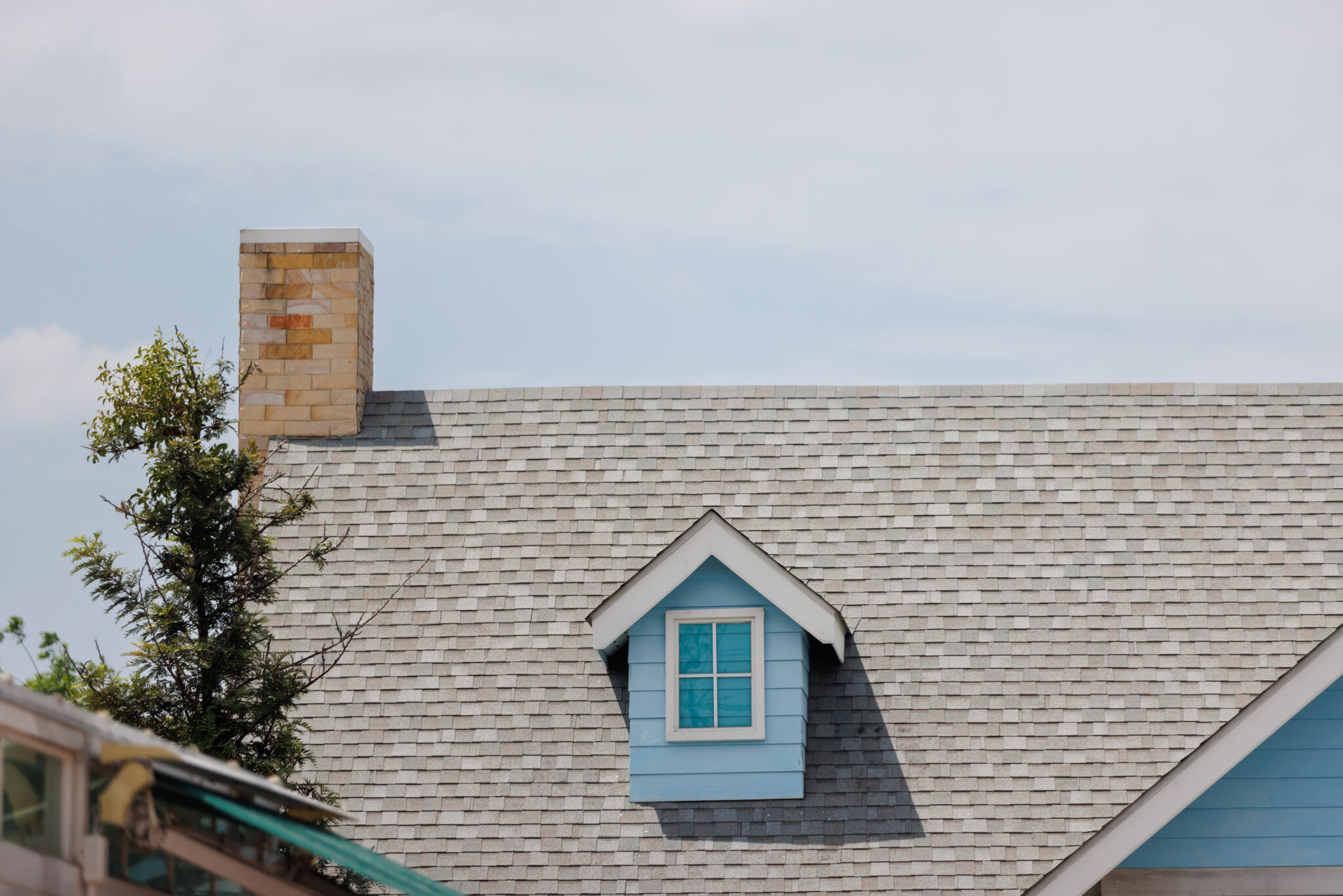 Asphalt shingle roof on a home with small attic window and brick chimney