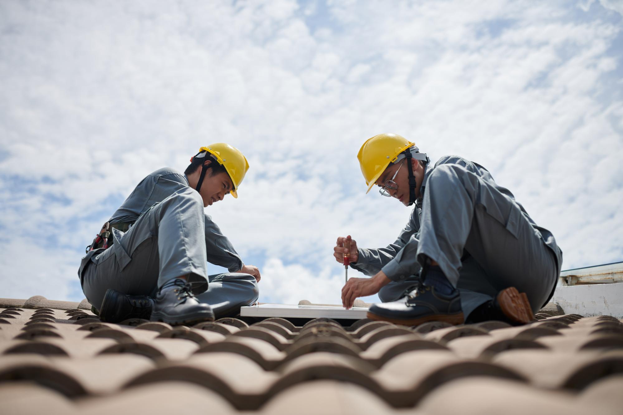 A pair of roofers carefully work on a Spanish tile roof.
